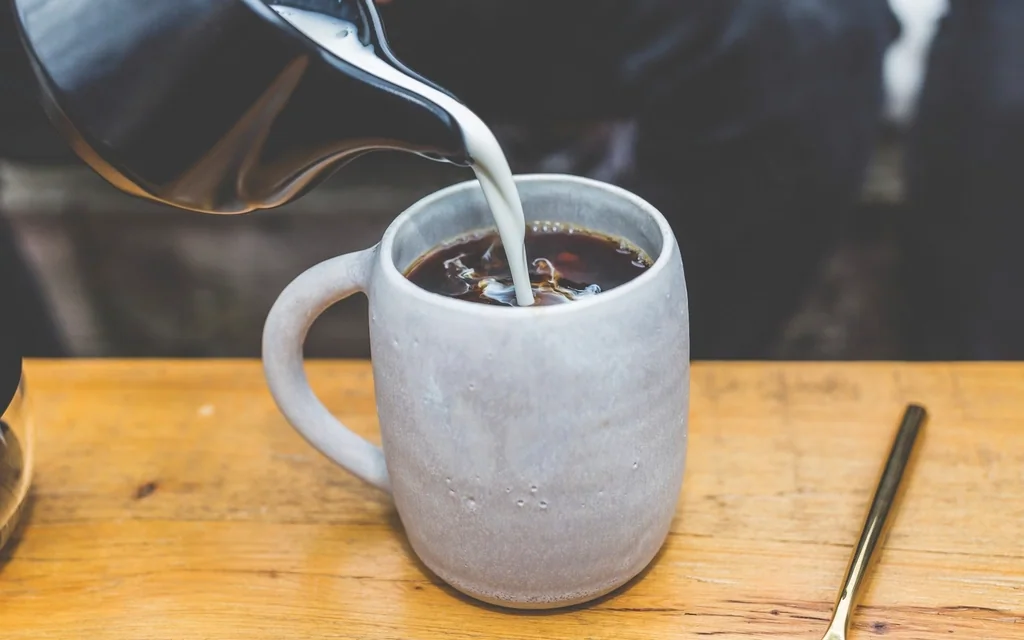 Milk being poured into a mug of coffee on a wooden table